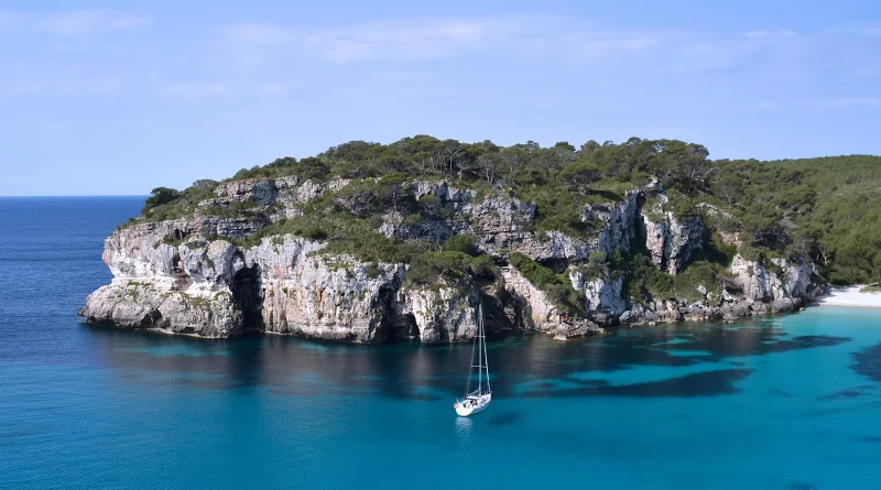 Cala Macarella Menorca with yachts, turquoise water and limestone cliffs