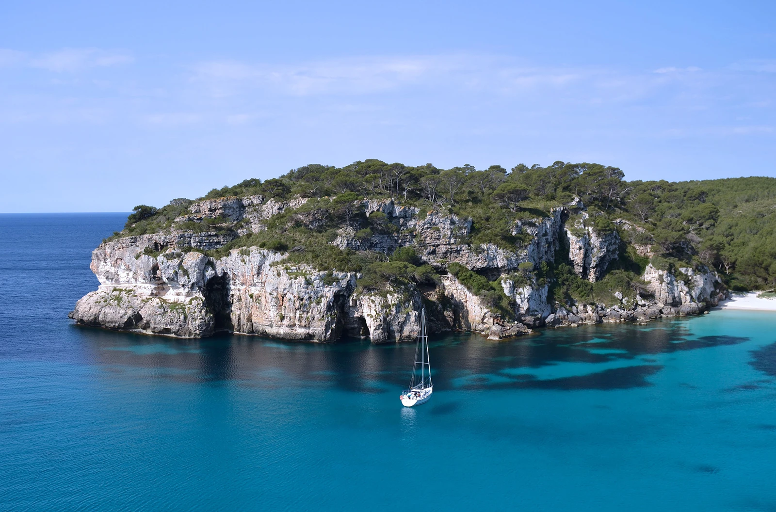 Cala Macarella Menorca with yachts, turquoise water and limestone cliffs