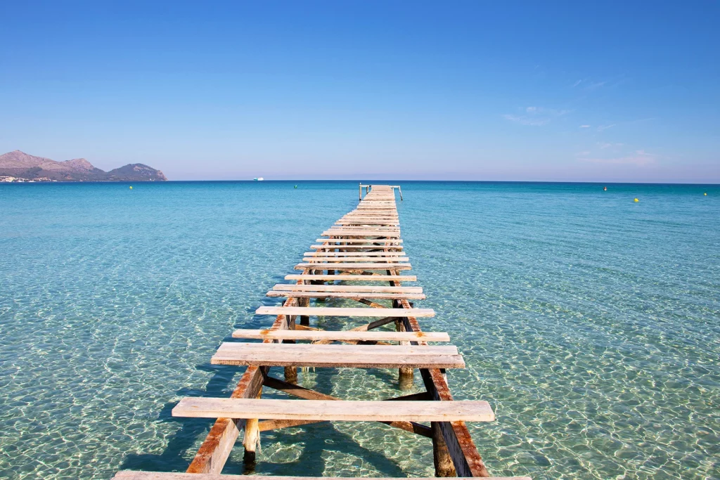 Playa de Muro beach in Mallorca with clear shallow water and a wooden pier